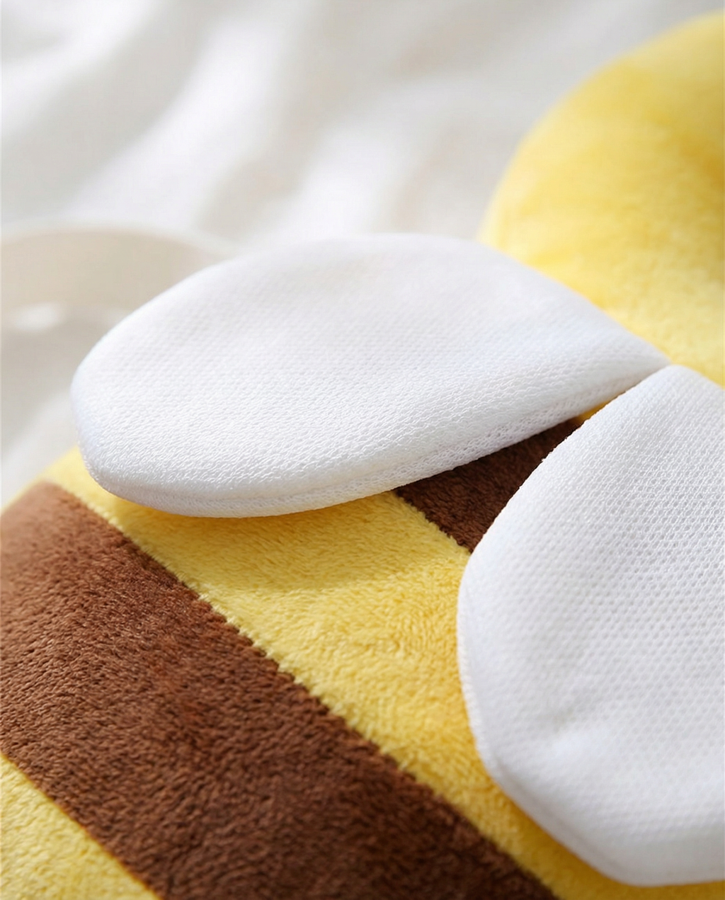 Close-up of the white wings and striped plush body of the bee cushion