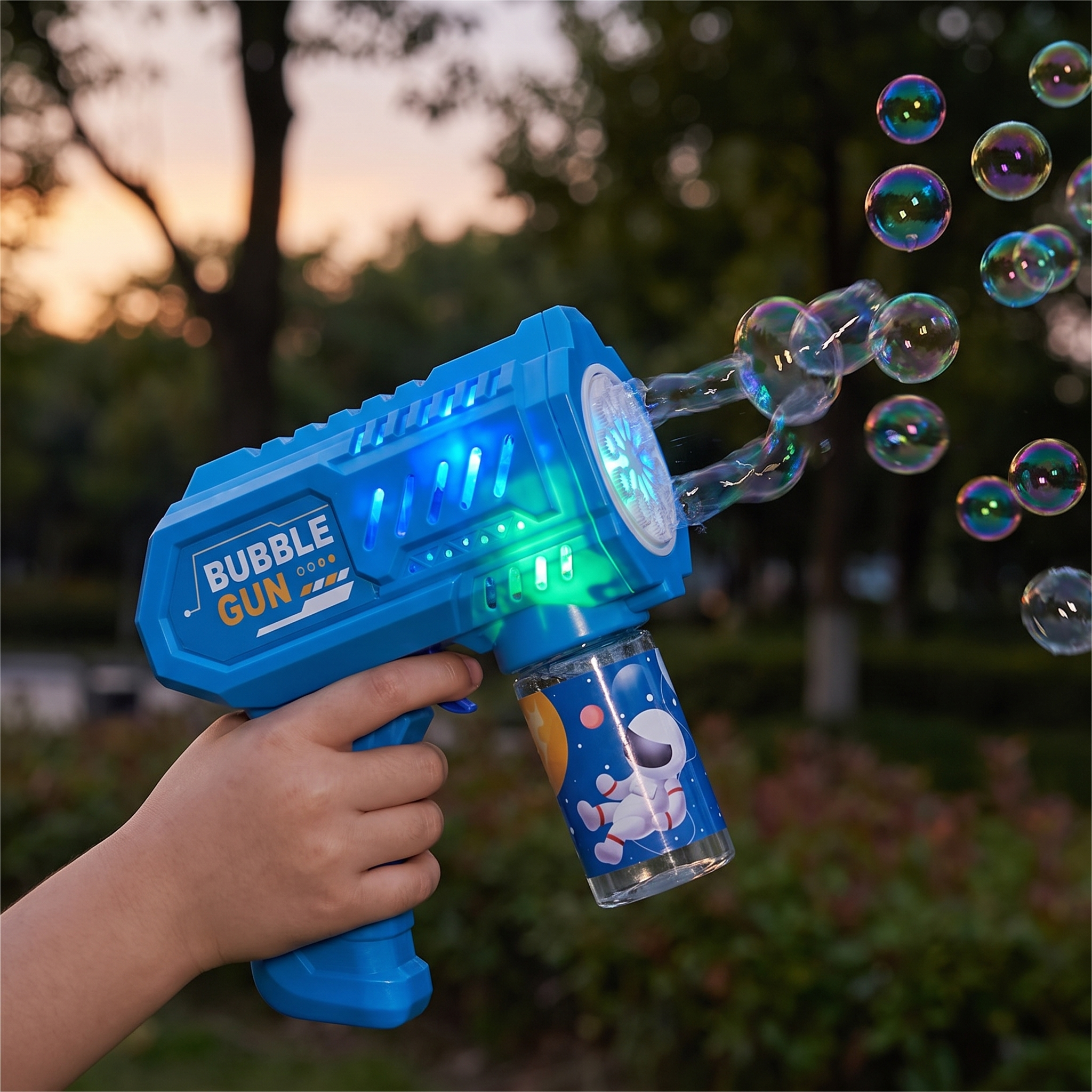 Blue bubble gun with glowing LED lights held in a child's hand at dusk, bubbles floating in the air